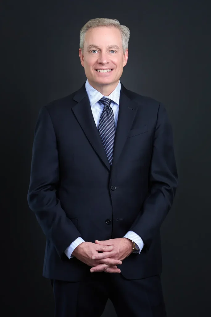 Professional studio headshot of a gray-haired businessman in a navy suit and tie.